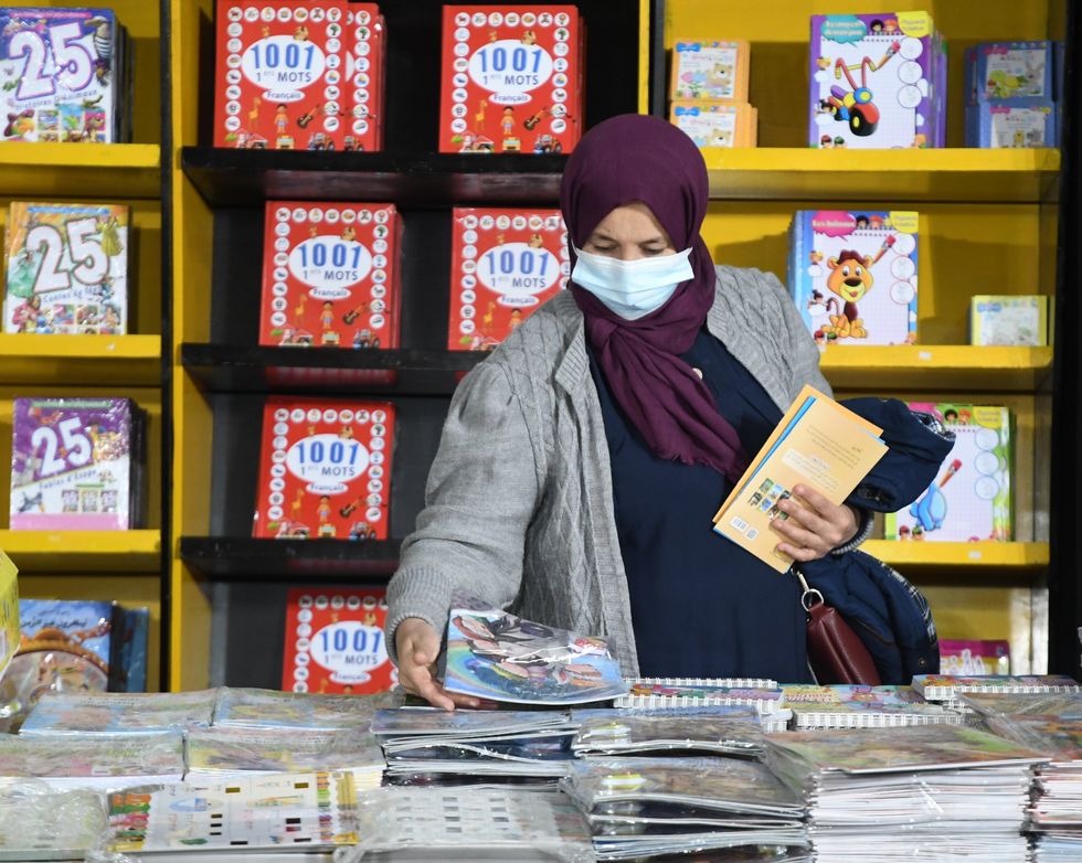 A woman in a headscarf and medical mask looks through a stand of childrens books