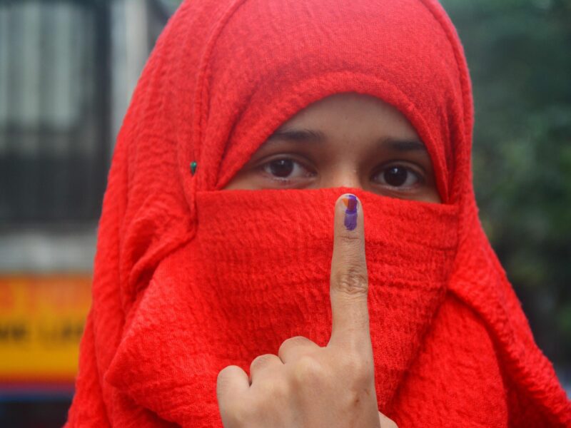 a woman in a red head scarf holds up her finger with ink on it