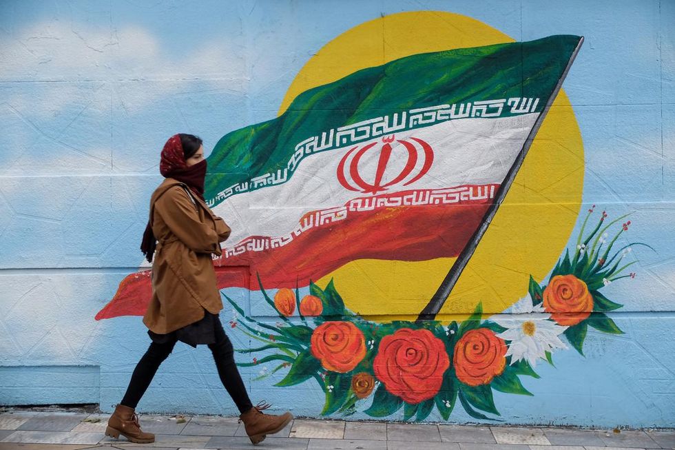 A woman in Tehran walks past a mural of an Iranian flag
