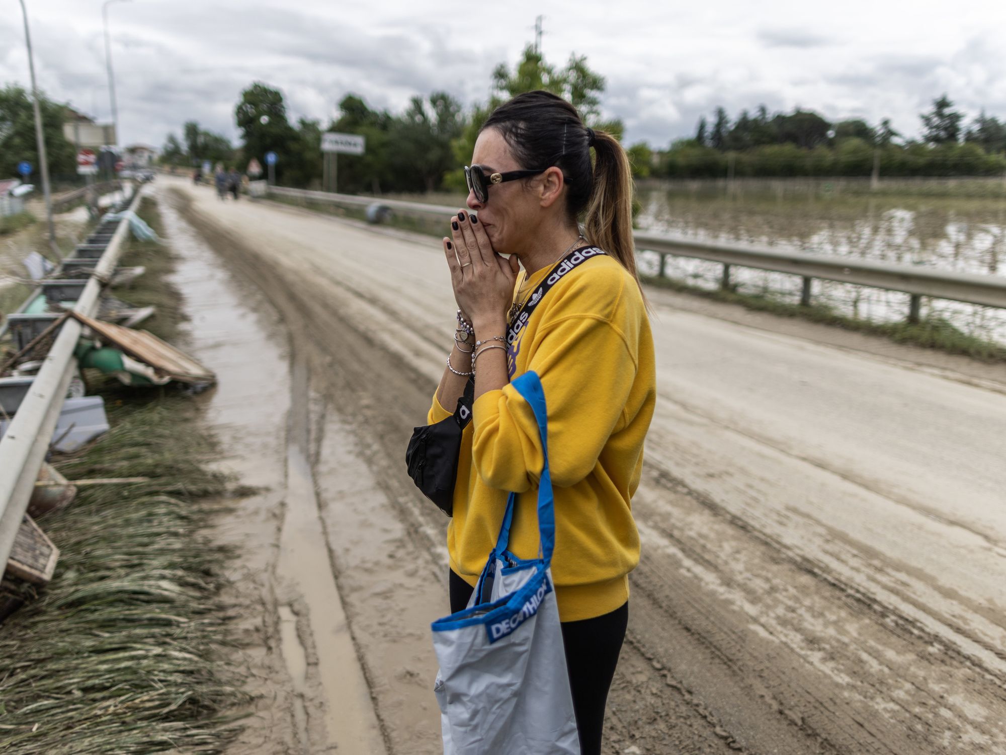 A woman in yellow stands crying on a bridge surrounded by floodwater