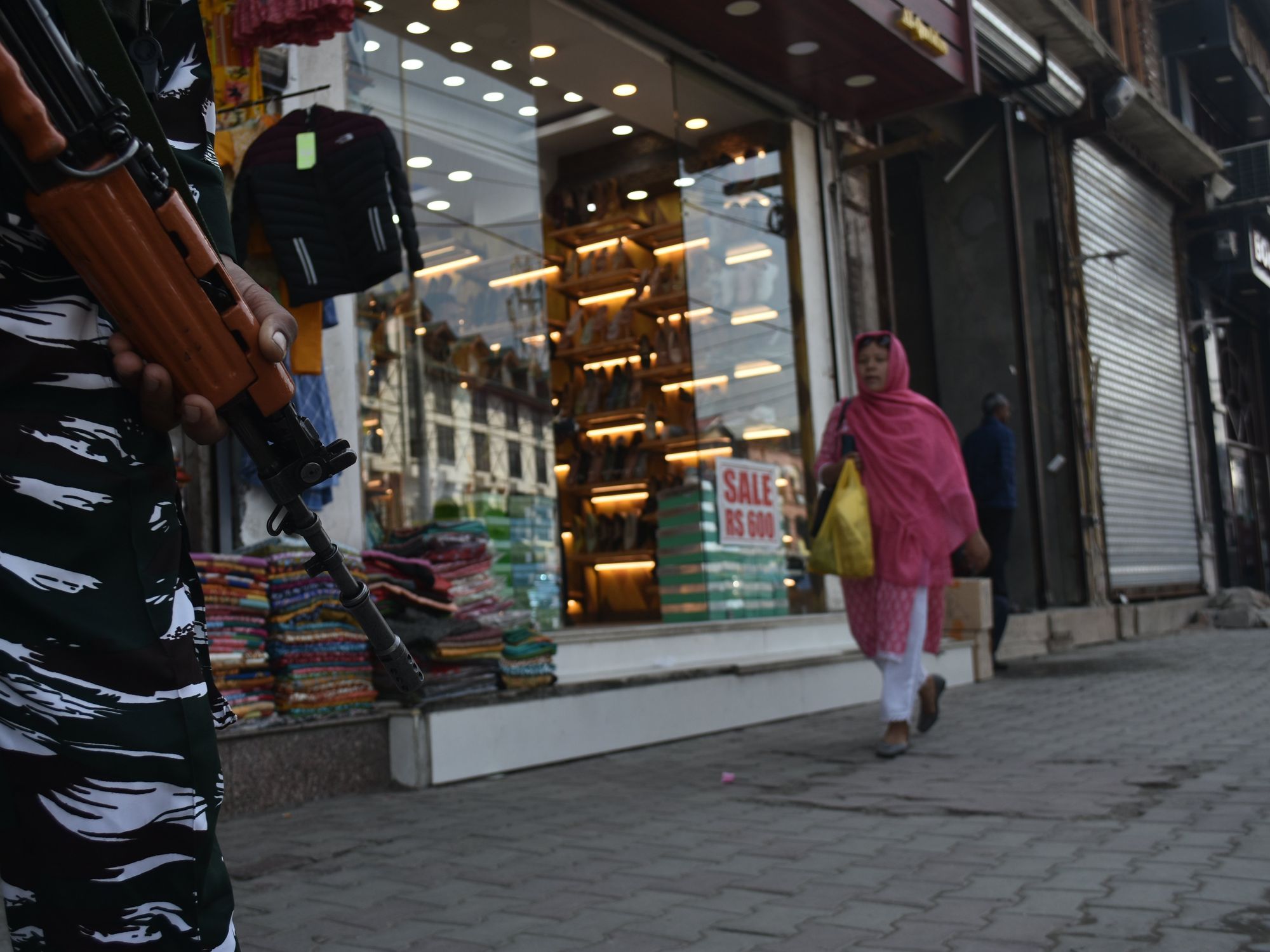 A woman is walking in the distance while a person holds a military-style gun close up
