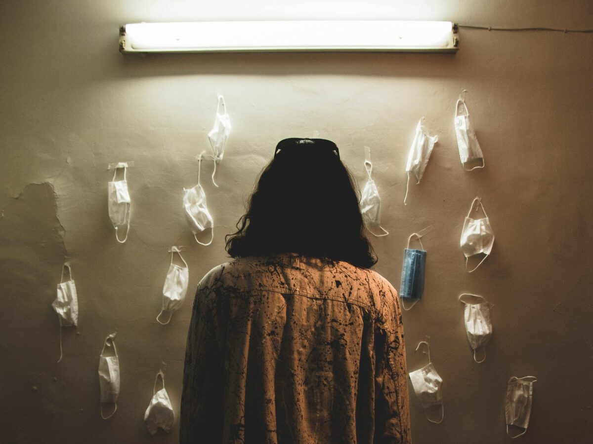 A woman seen from the back stares at masks pinned on a wall.