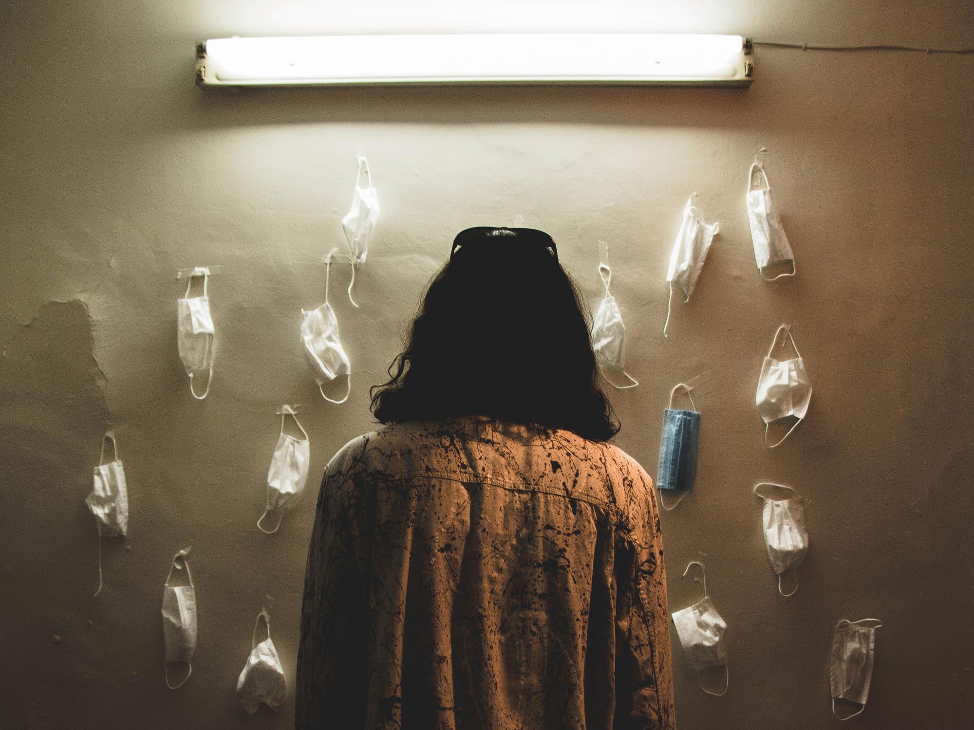 A woman seen from the back stares at masks pinned on a wall.