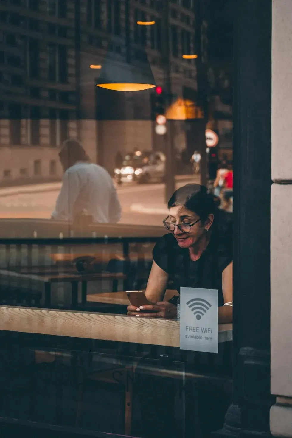 A woman uses her smartphone inside a shop, seen from the outside with a "Free WiFi" sticker on the window