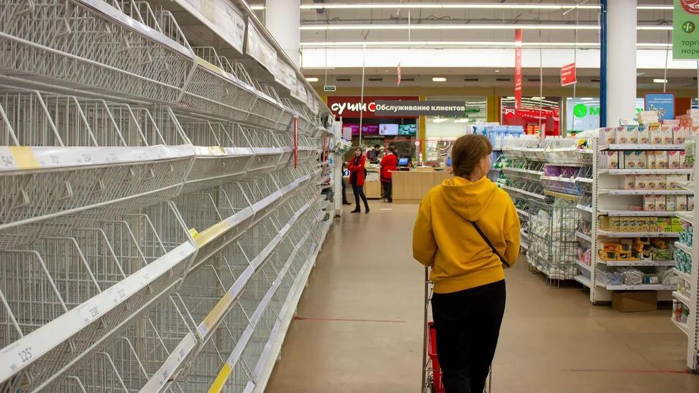 A woman walks by empty shelves in a supermarket in Moscow
