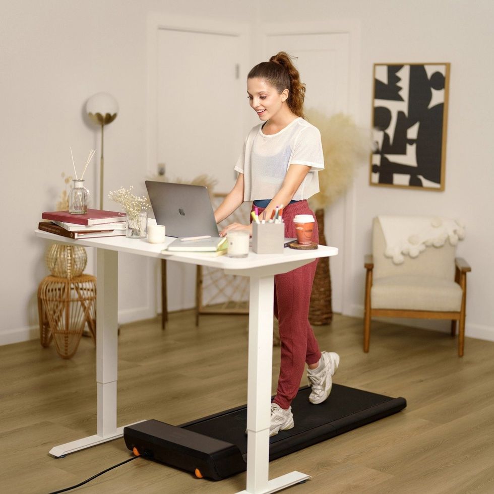 A woman walks on a treadmill in an office while working on her laptop
