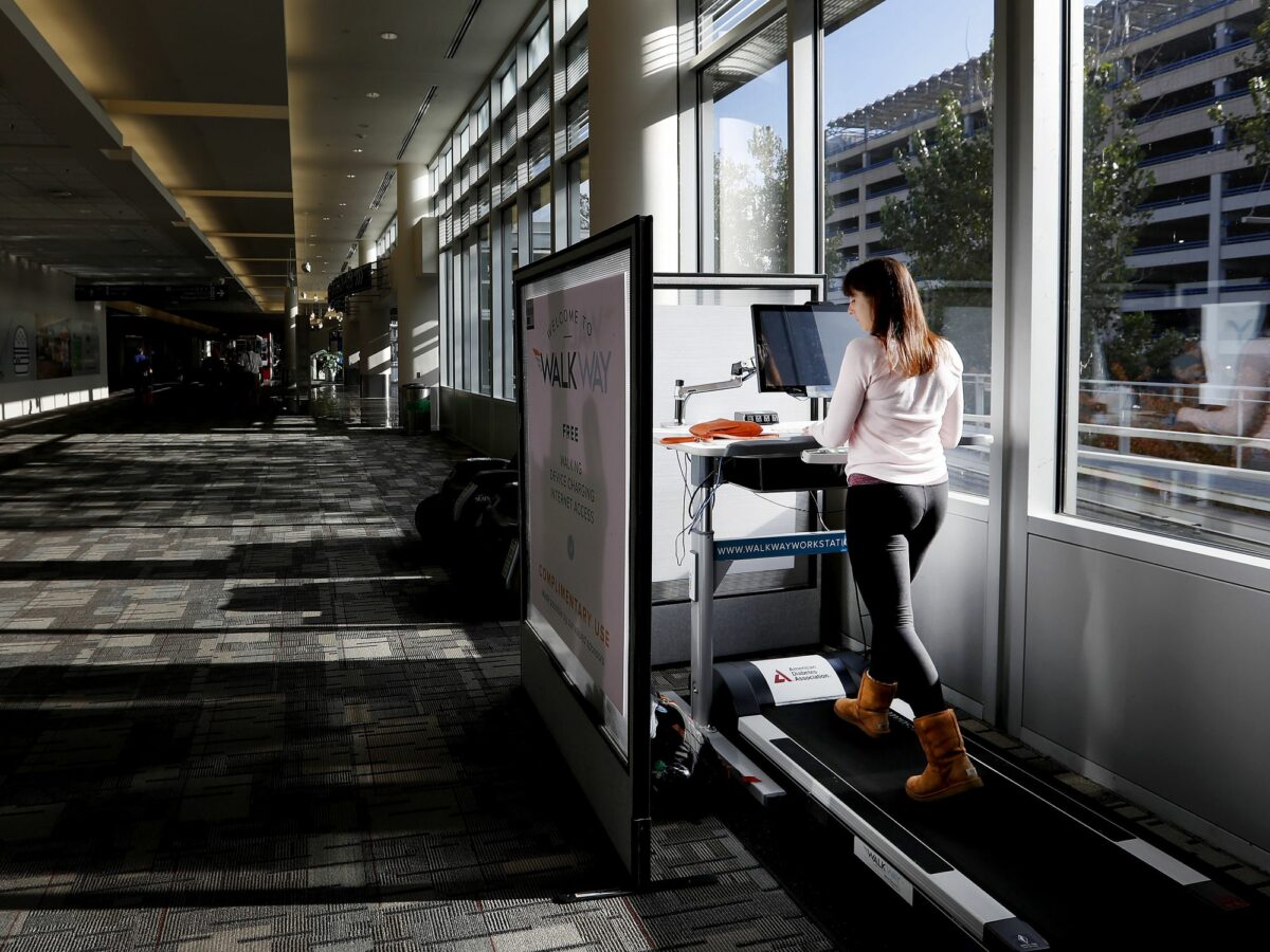 A woman walks on a treadmill while working on a computer