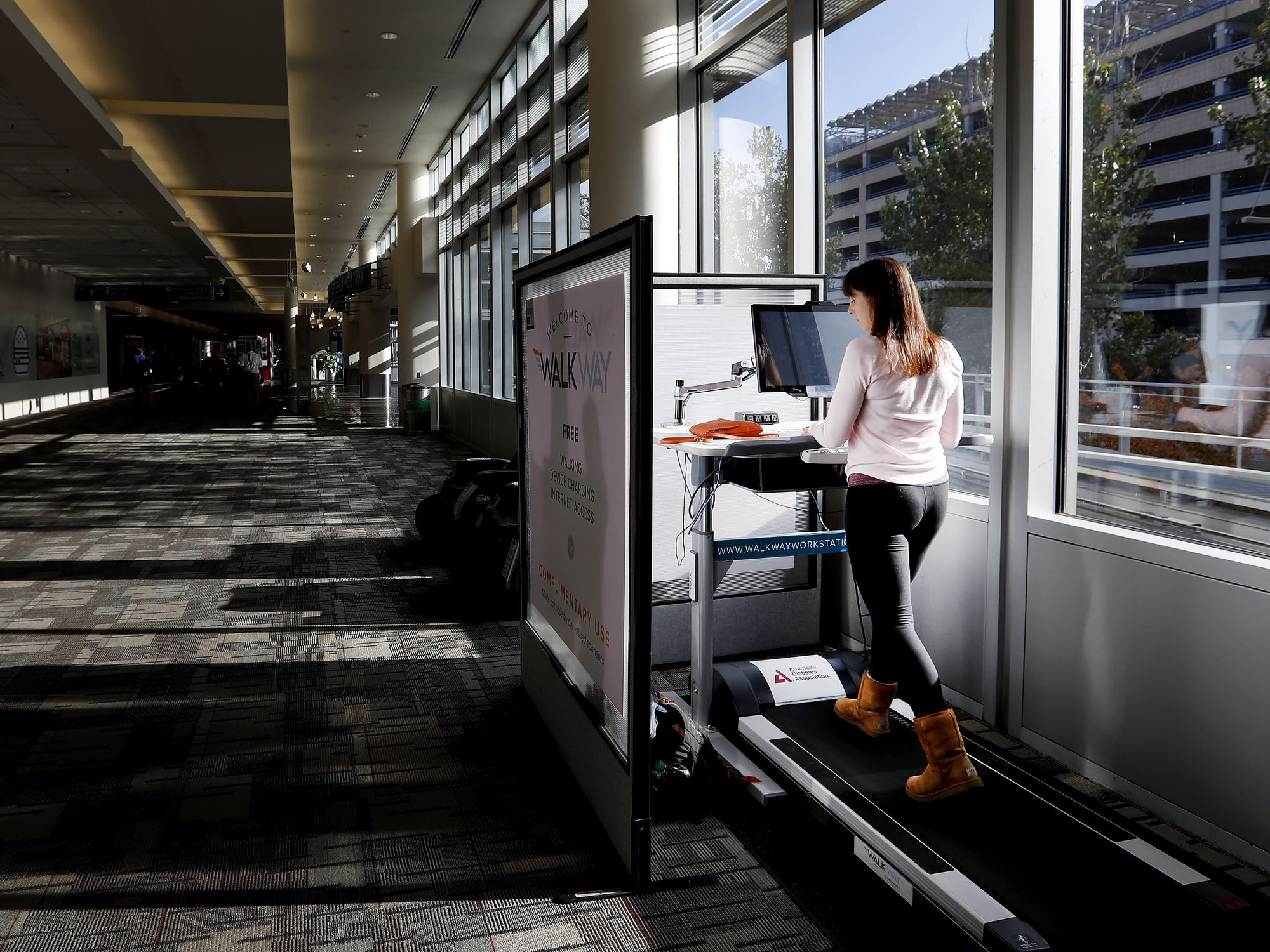 A woman walks on a treadmill while working on a computer