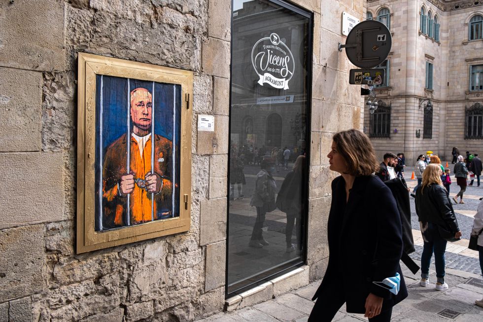 A woman walks past a painting of Putin behind bars.
