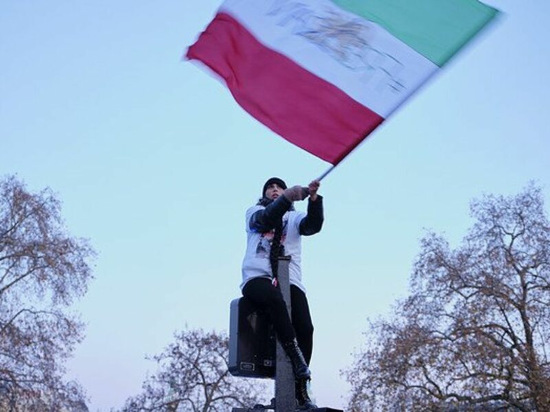 A woman waves the Iranian flag sitting on a trafifc light.