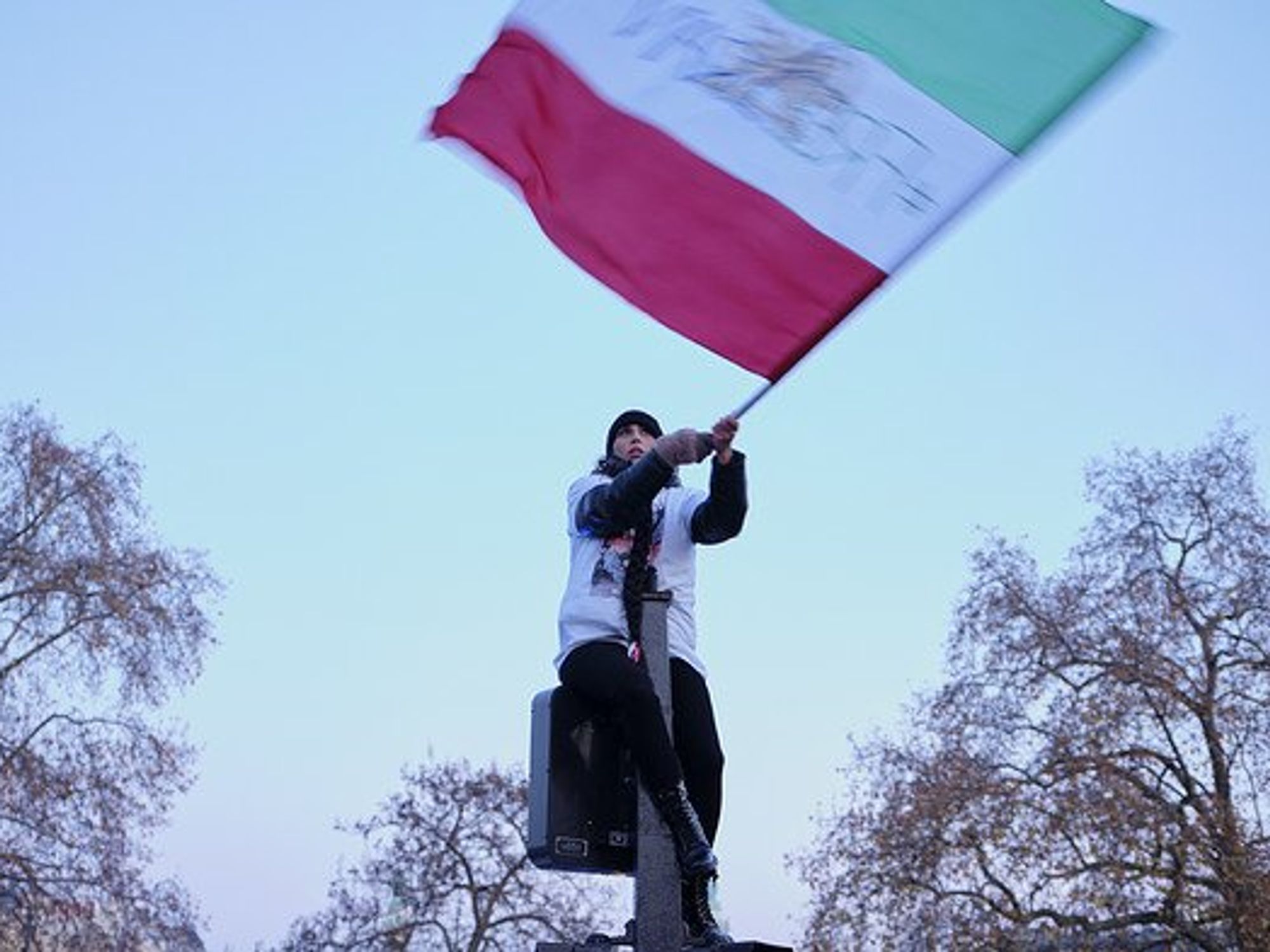 A woman waves the Iranian flag sitting on a trafifc light.
