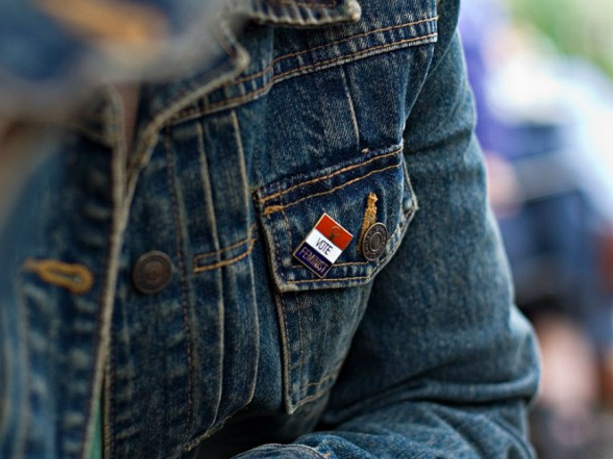 A woman wears a feminist pin on her jean jacket.