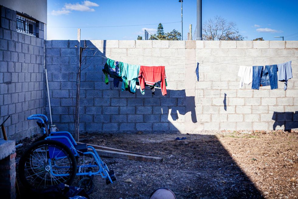 A yard walled by brick containing a wheelchair, a clothes line and debris