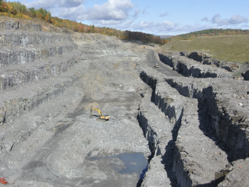 A yellow digger is dwarfed by the Lac des Iles graphite mine in Quebec