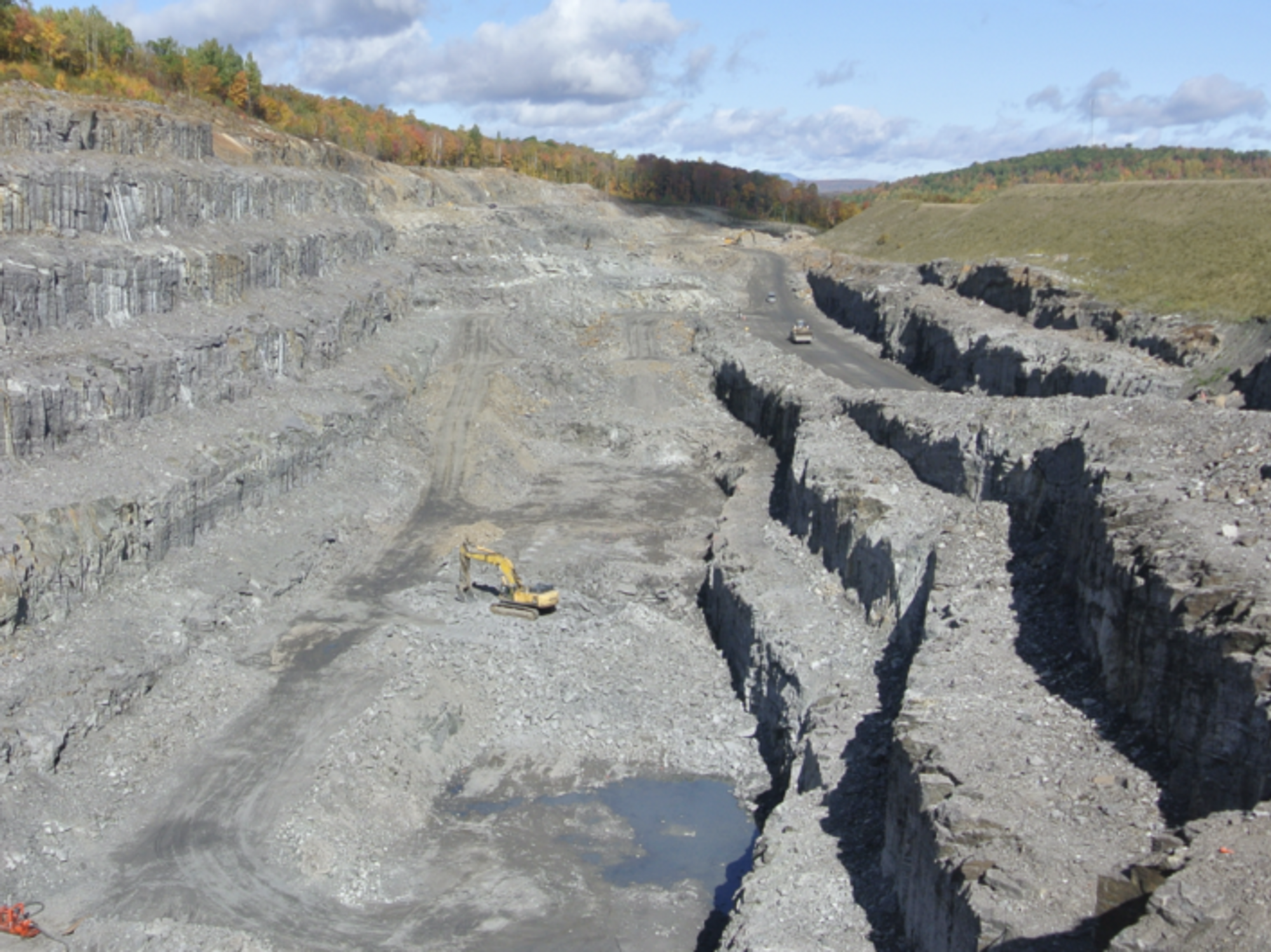 A yellow digger is dwarfed by the Lac des Iles graphite mine in Quebec