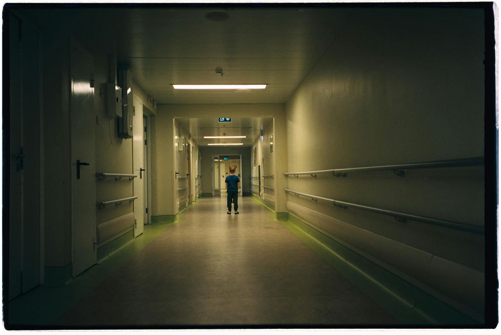 A young boy stands in a dark hospital hallway