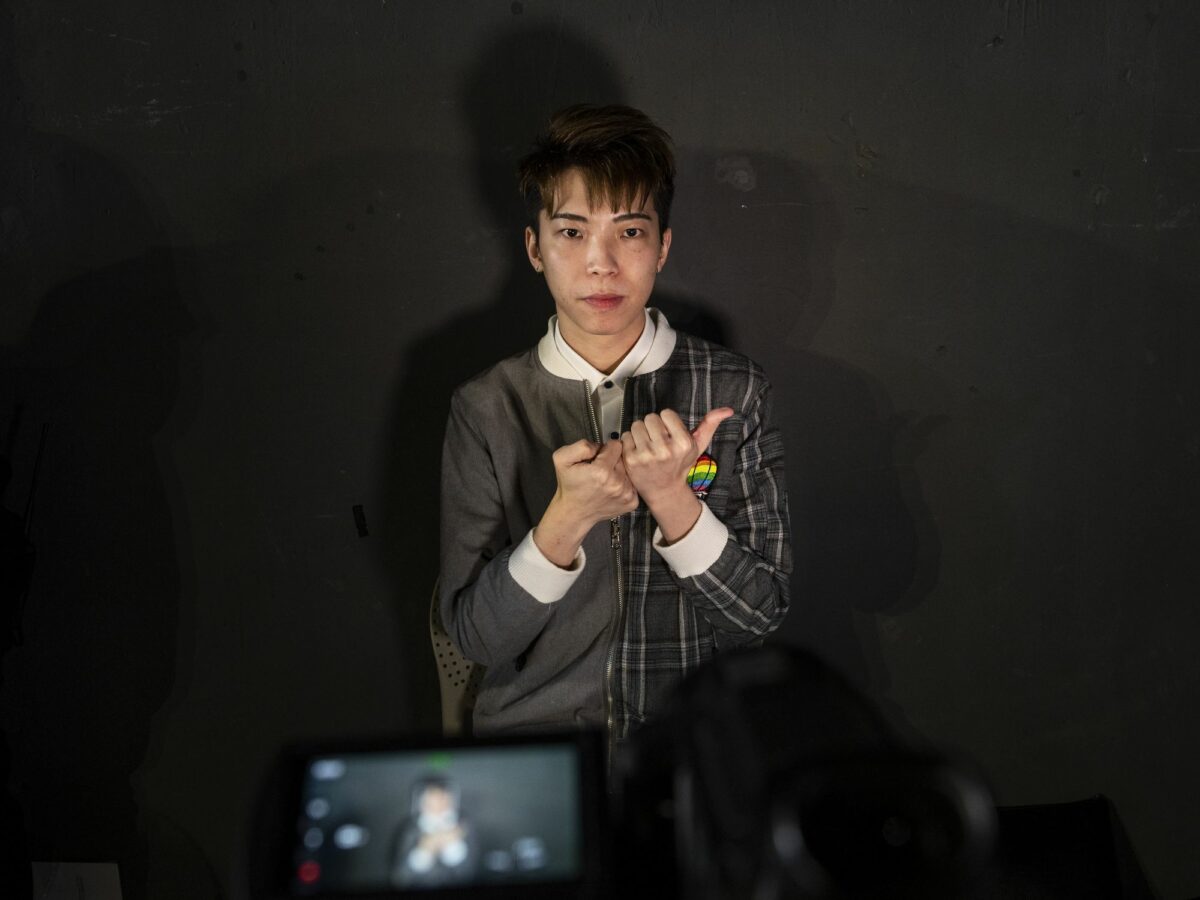 A young person signs to a camera infront of a black background