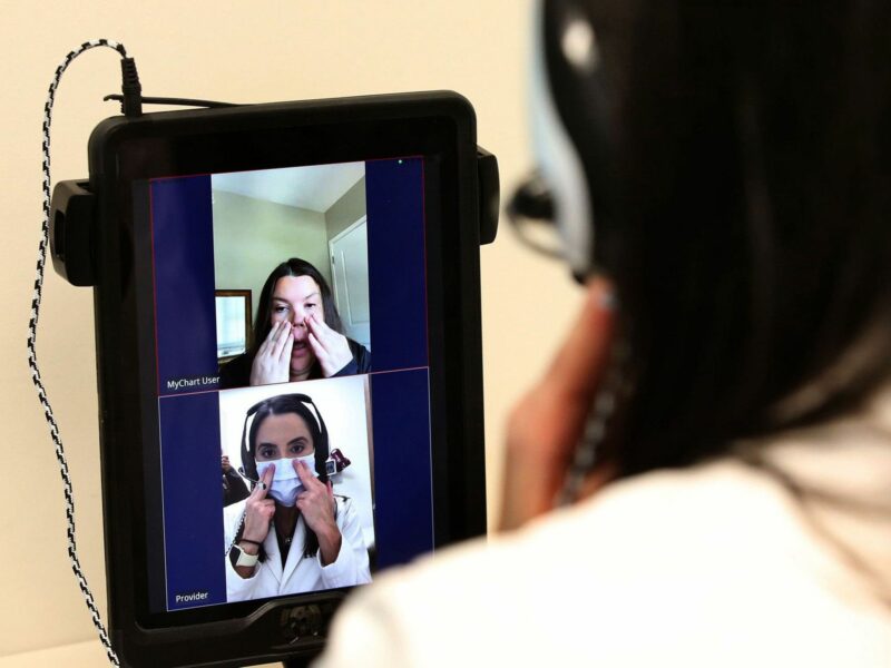 A zoom meeting between a medical provider with a mask and a patient takes place on a zoom meeting