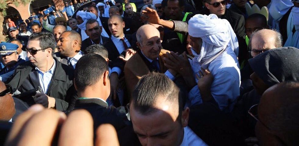 Abdelmadjid Tebboune moving through a crowd of supporters with security guards.