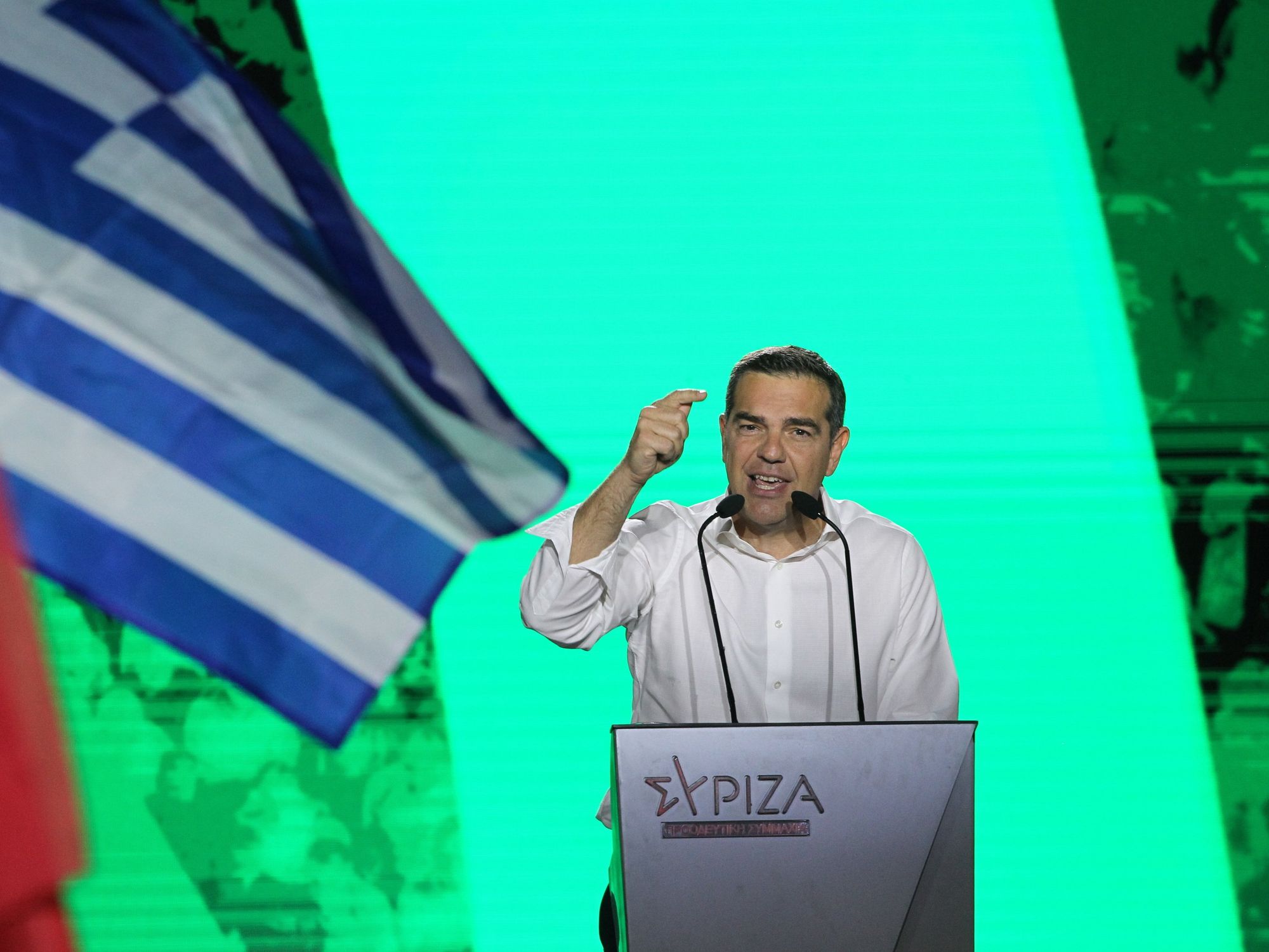 Alexis Tsipras speaks at a podium with a greek flag in the foreground