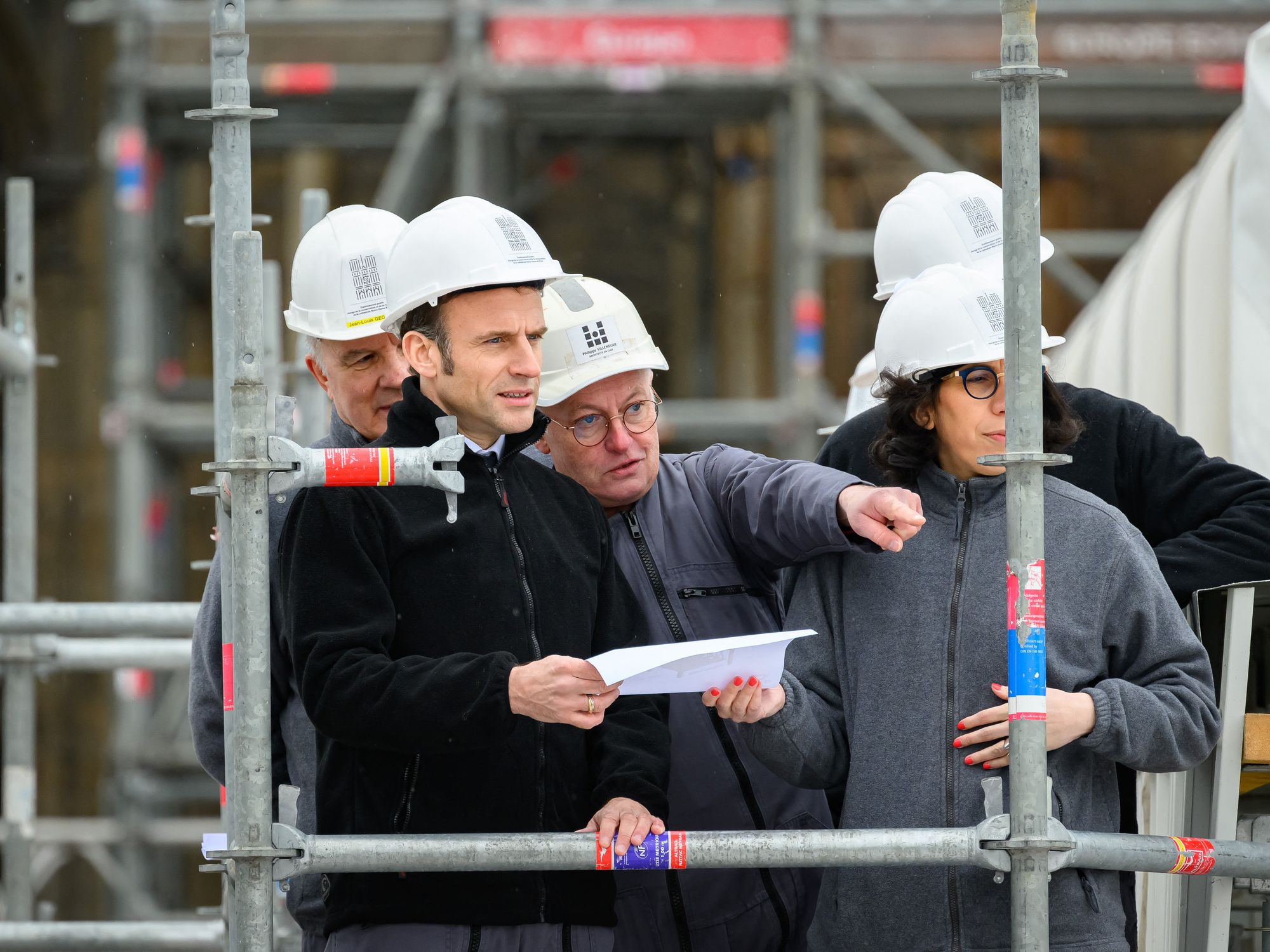 All wearing workers' helmets, ​French President Emmanuel Macron and Chief architect Philippe Villeneuve with French Culture Minister Rima Abdul-Malak install the last structural element of the stool of the fleche at the restoration site in Notre-Dame, Paris, April 14, 2023.
