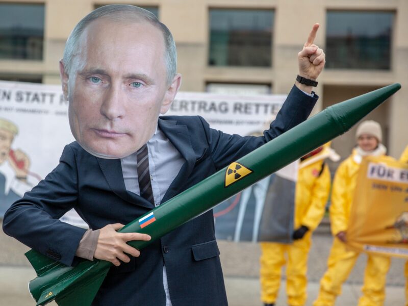 An activist wearing a Putin mask and a nuclear missile toy.