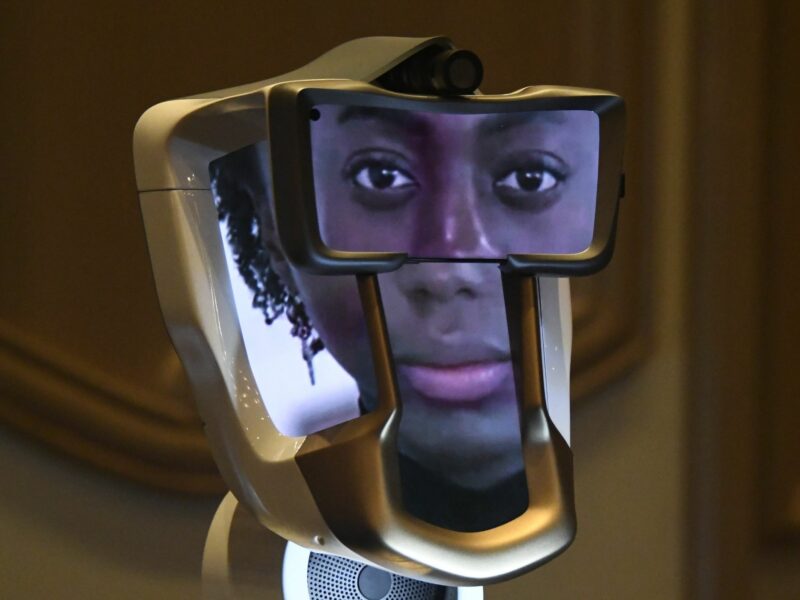 An AI face on 4 different screens with a camera at the top and a speaker at the bottom of the machine.