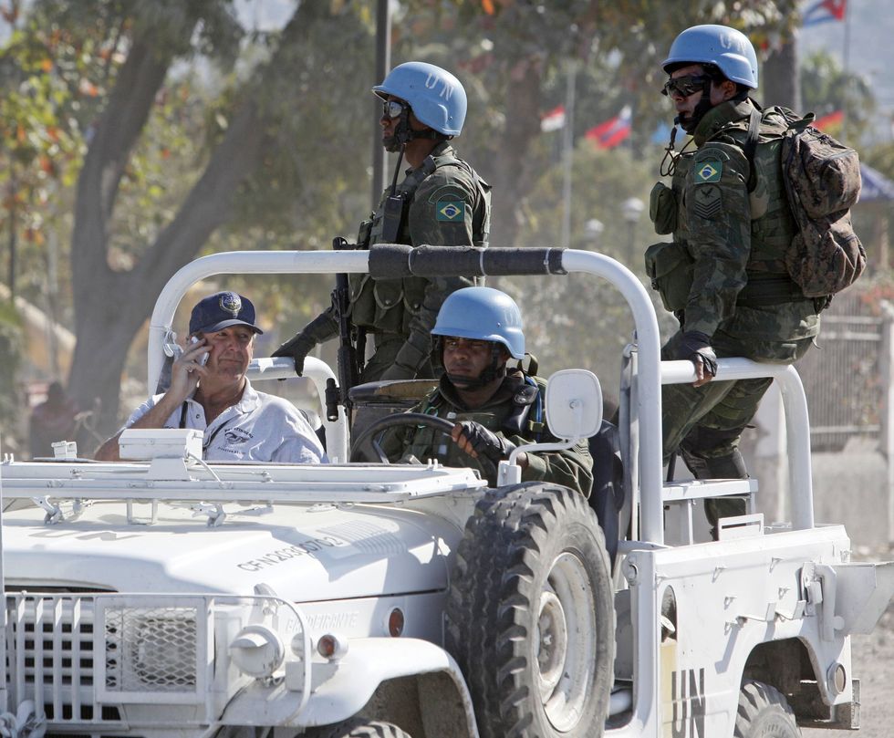 An aid worker sits in a white jeep with three UN troops in blue helments.