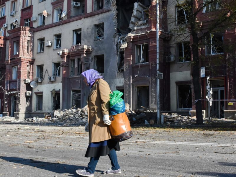 An elderly woman walks down the street by the apartment building that was damaged by Russian shelling in Zaporizhzhia.