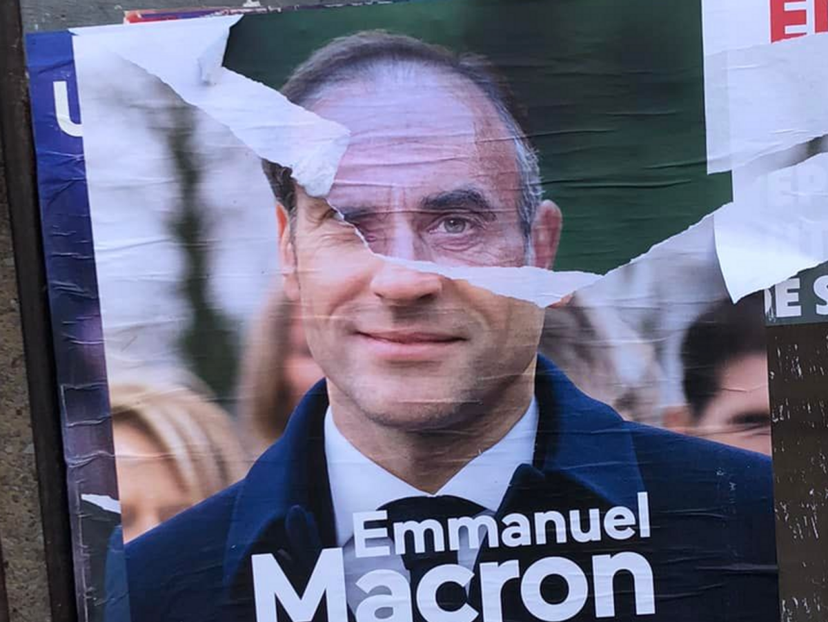 An electoral poster showing Eric Zemmour's head showing from beneath a torn campaign poster of Emmanuel Macron.