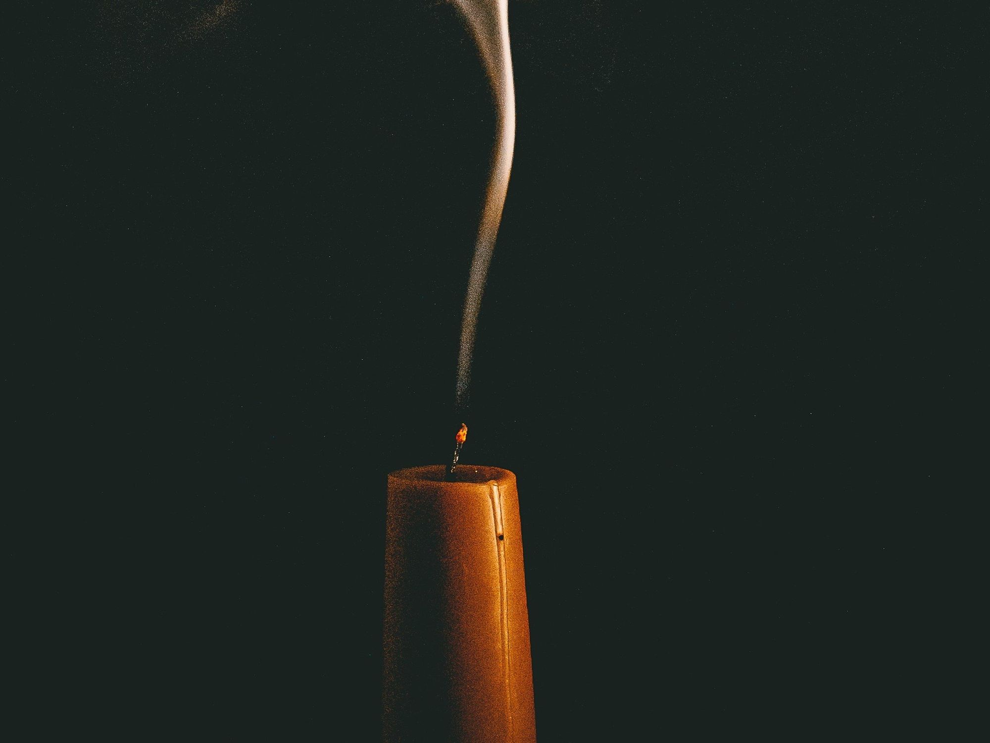 An image of an orange candle burning, with smoke on top of it.