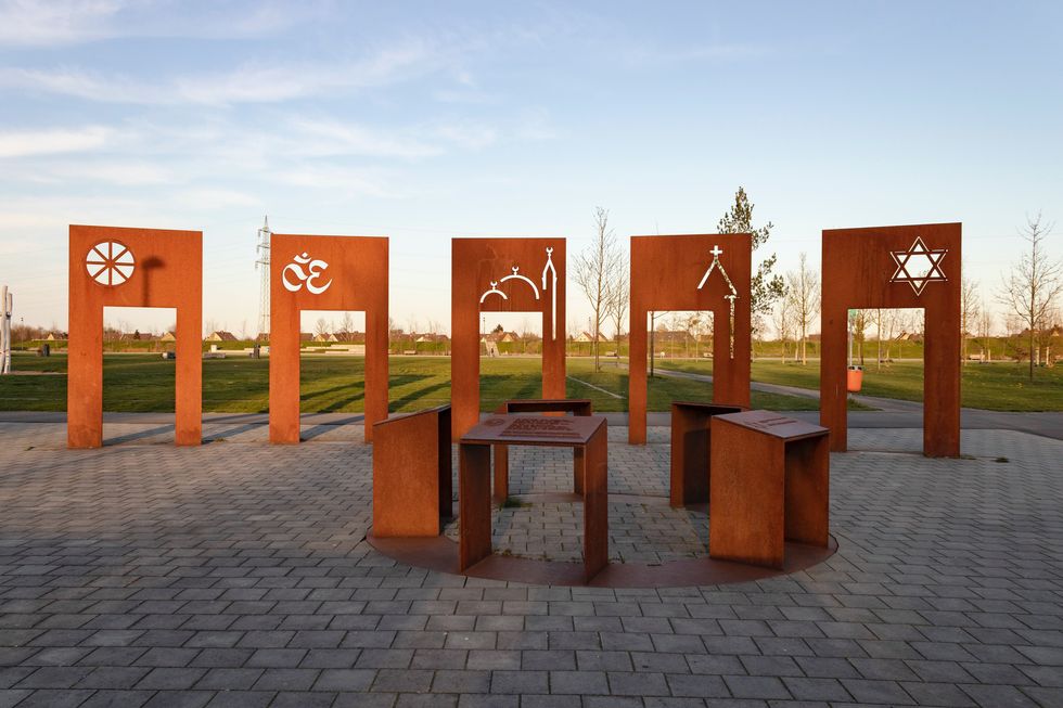An image of orange sculptures, outside, representing different religions.
