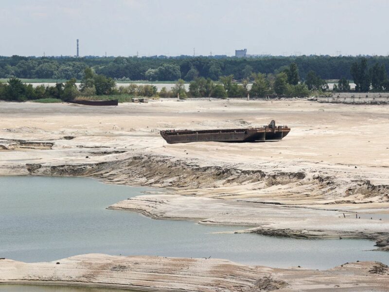 An image of the dried up reservoir, rusted vehicles banked on the sandy earth.