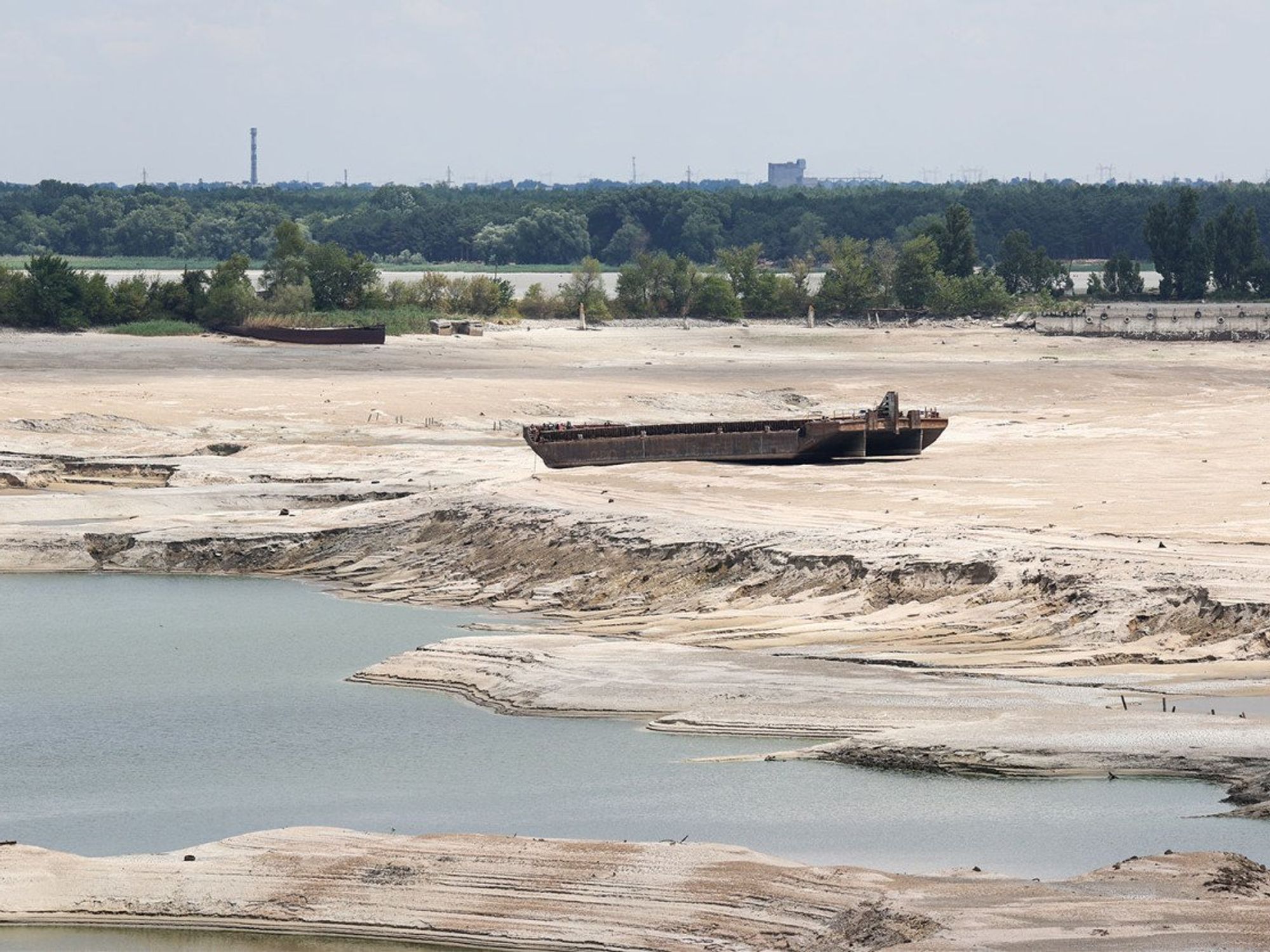 An image of the dried up reservoir, rusted vehicles banked on the sandy earth.