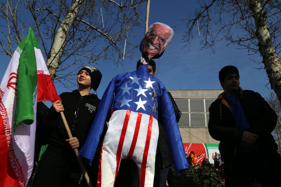 An Iranian man holds a symbol of the USA flag and United States President Joe Biden while gathering to mark the 45th anniversary of the Islamic Revolution in Tehran.