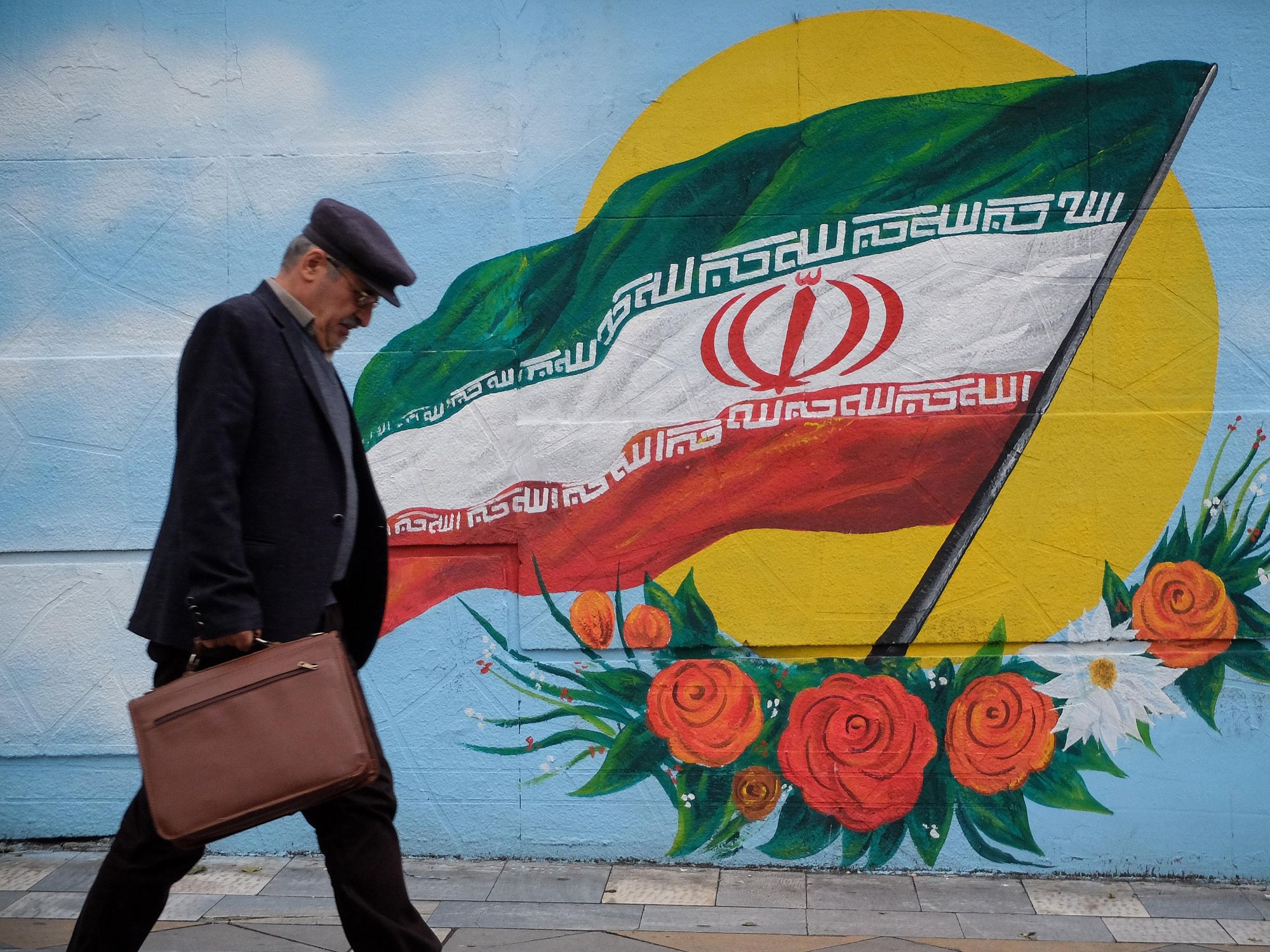 An Iranian man walks past a painting of the Iranian flag in Tehran.
