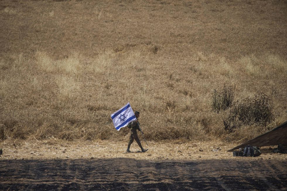An Israeli Defence Forces soldier walking holding the Israeli flag at the Gaza border