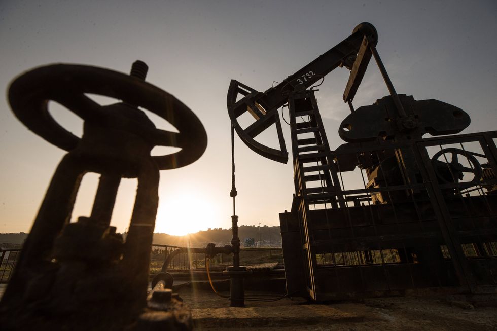 An oil rig silhouette at dusk in an arid region, with the sun setting in the background