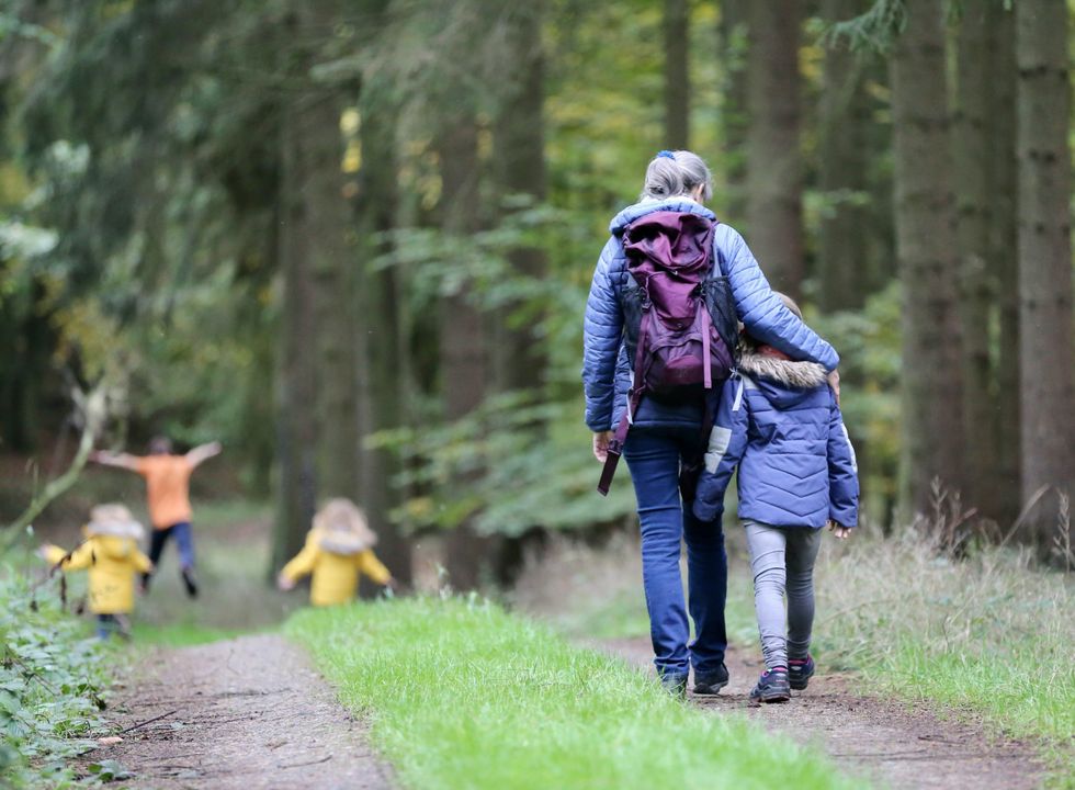 An older lady has her arm around a young boy as they walk down a path in the woods.