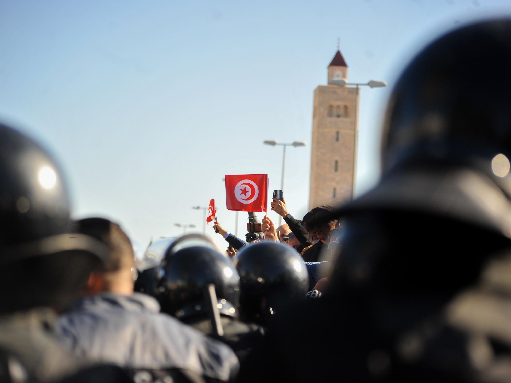 Anti-riot officers standing next to demonstrators holding the Tunisian flag in front of the Parliament in Tunis