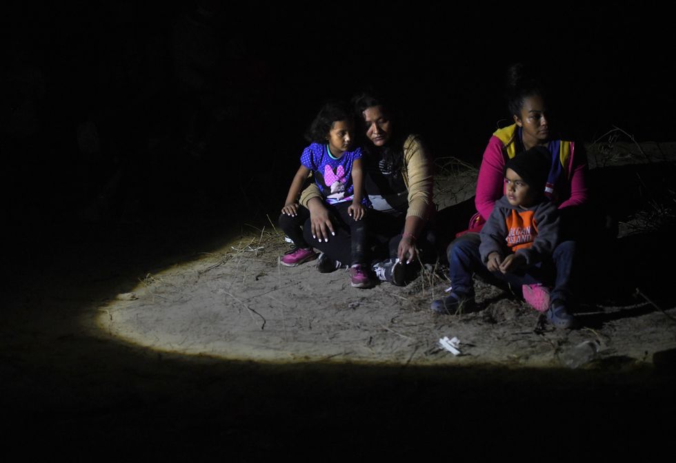 Asylum-seeking migrants with children sit on the river bank and wait as Texas Rangers escort them into custody after they crossed the Rio Grande River illegally into the US at the border with Mexico in Roma.