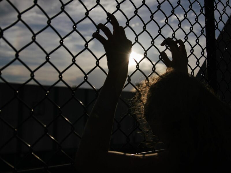 Backlit photo of a woman holding onto a fence