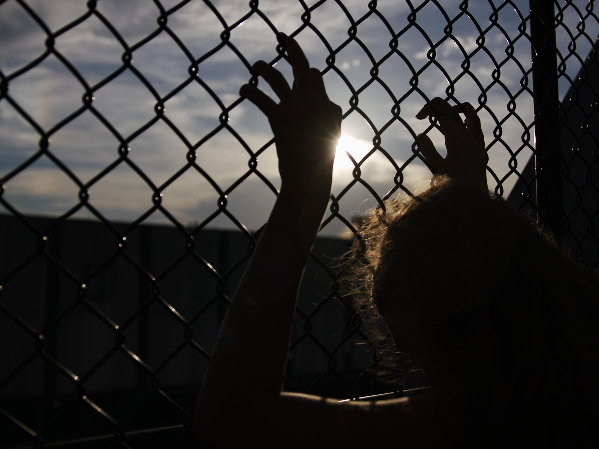 Backlit photo of a woman holding onto a fence
