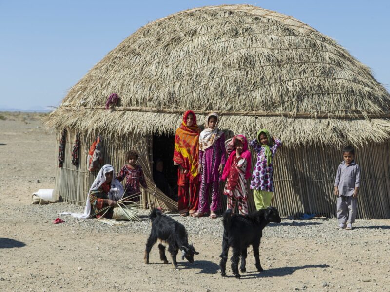 Baloch or Balunch family outside of their house with 2 black sheep grazing the land.