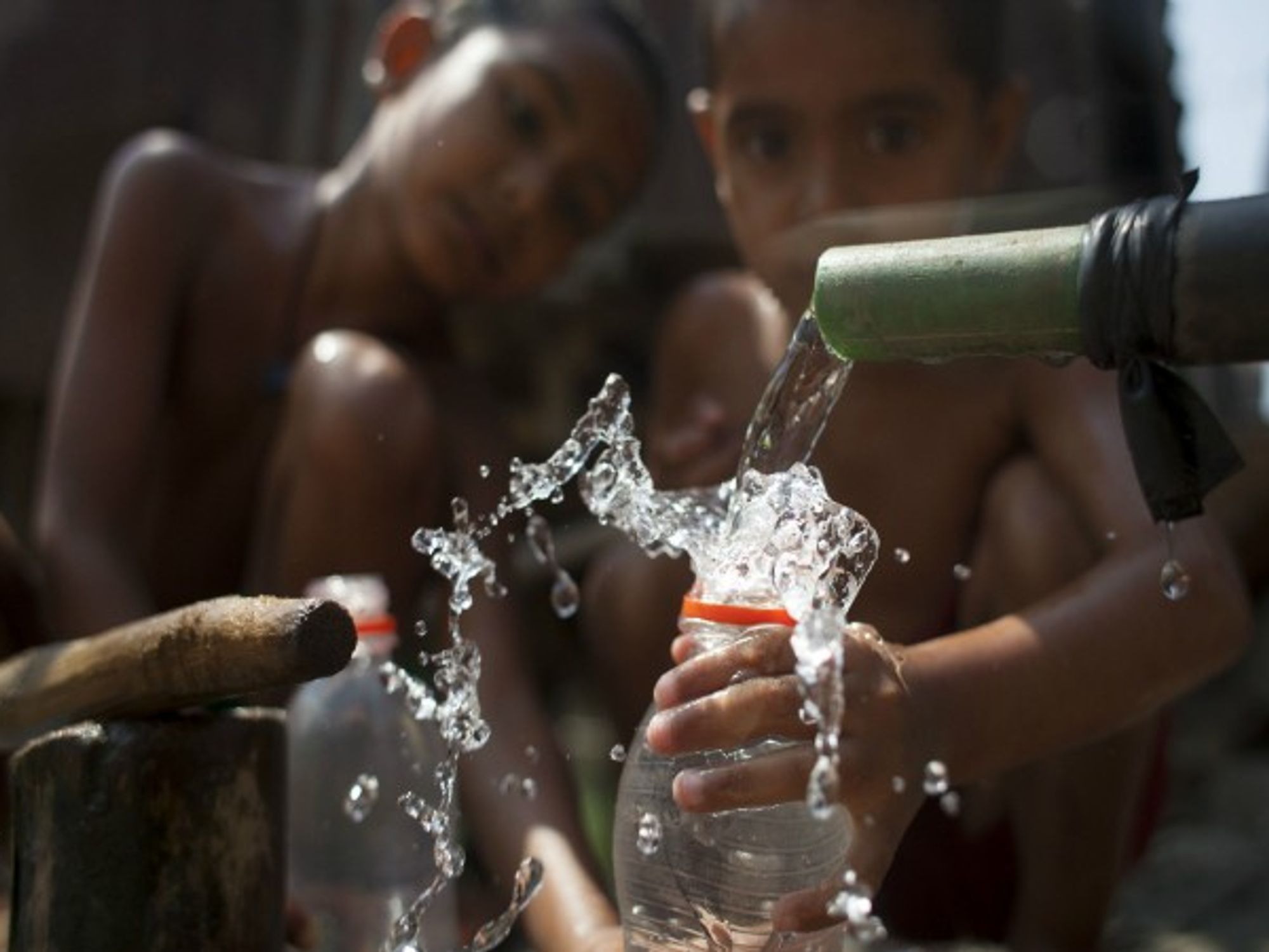 Bangladeshi children taking a bath by collecting supply water beside a road in Dhaka