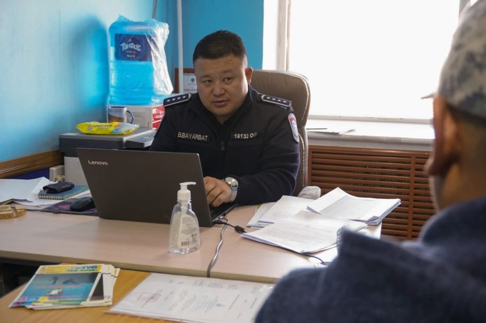 Bayarbat Batsaikhan, seated in his office at the police headquarters in Umnugovi province, takes a statement from someone who says they were scammed online.