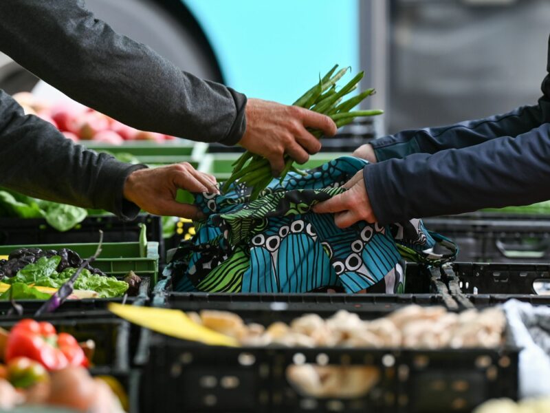 Beans being packed into a customers bag at the weekly market. There are other vegetables on the table as well.