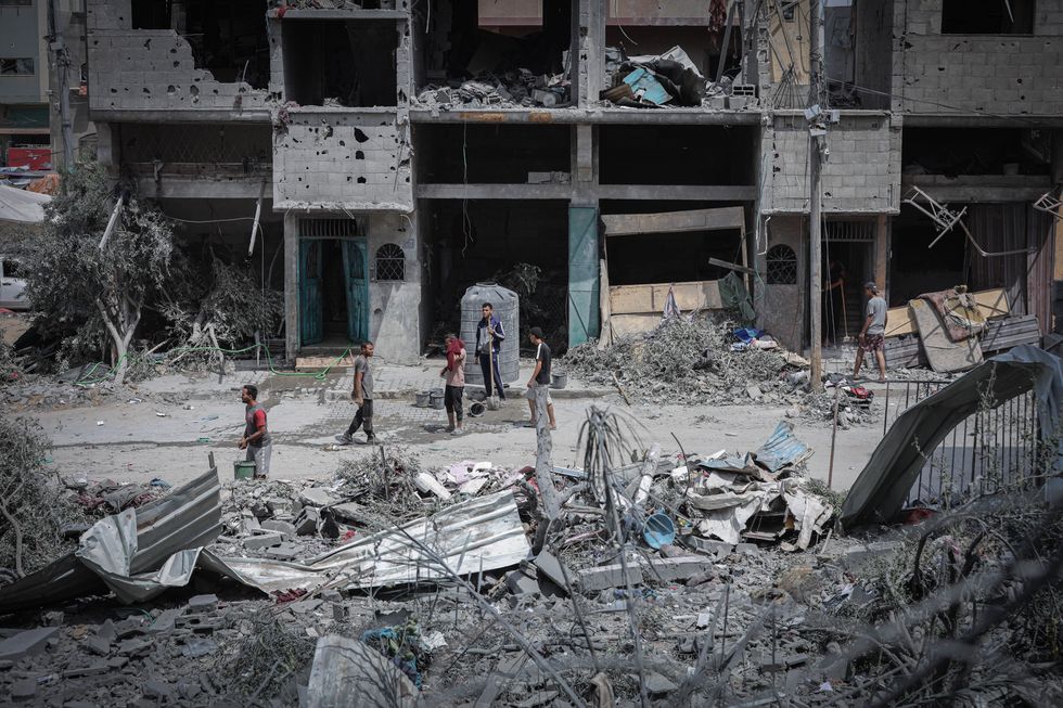 Behind a line of rubble and in front of a destroyed building 6 people seem to be going about their business