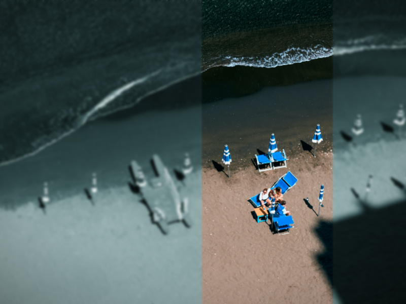 Bird's eye view of a beach in Naples, with blue parasols and people sat on chairs