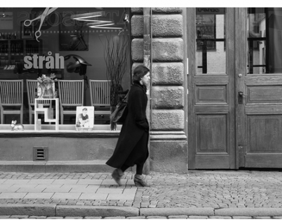 Black and white photo of a woman walking past shop windows in Lund, Sweden